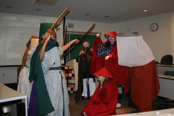 Several actors perform a skit based on historic Japanese theatre in a university classroom during an anime convention, all dressed in clothing inspired by historic Japanese fashion but playing fruits and vegetables about to battle each other.