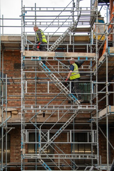 Two workmen climbing the scaffolding in front of the Victorian bellfoundry.