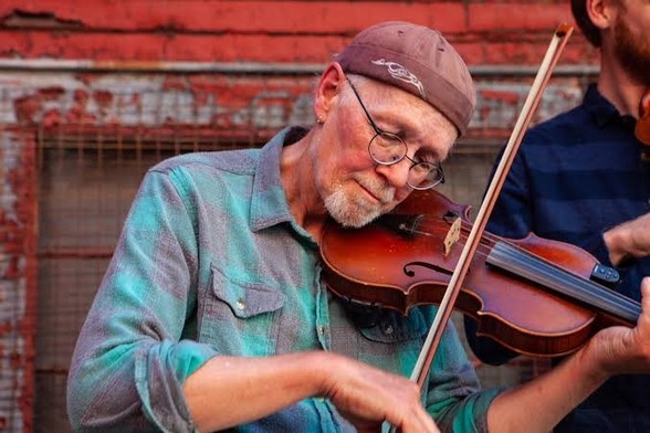 The picture of fiddler Pete Sutherland, eyes closed, skull cap hat, wire rimmed glasses, white, faint goatee, wearing a blue and turquoise shirt, sleeve rolled up on his right bowing hand, his fiddle tucked under his left cheek, the side of an old red barn behind him and to his left the edge of another fiddler. 

Pete, with the aid of a physician, took his own life. He was wracked with pain and had no chance of recovery from his latest  bout with cancer.