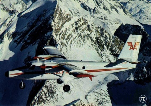 A twin engined prop plane flies in and out of the shadows around snowy mountains
