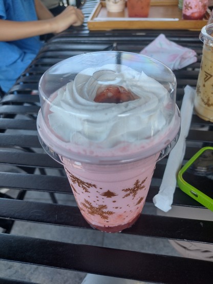A takeout cup of a strawberry cream drink, featuring the strawberry syrup at the top surrounded by whip cream