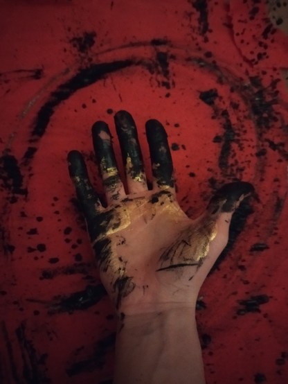A picture of a hand with gold and black ink, on a red backdrop.