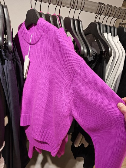 A bright magenta colored knitted sweater hanging on a rack in a store.