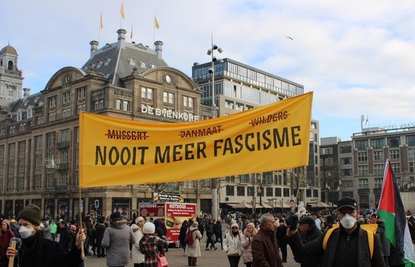 Banner held up by people wearing facemasks with the names 'Mussert', 'Janmaat', and 'Wilders', all struck out, with below that the text 'Fascism, never again' (in Dutch). One person holds a Palestinian flag.