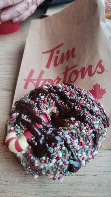 Tim Hortons doughnut absolutely covered in red, green and white sprinkles, a red and white striped candy cane & drizzled chocolate