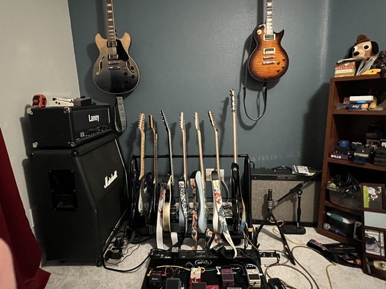 Room with a bunch of guitars and a couple of amplifiers.
