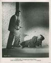 a man points a revolver at a grounded man in an alleyway. From the 1954 film Naked Alibi.