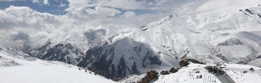 Panoramic view of a ski slope and snow covered mountains around it.