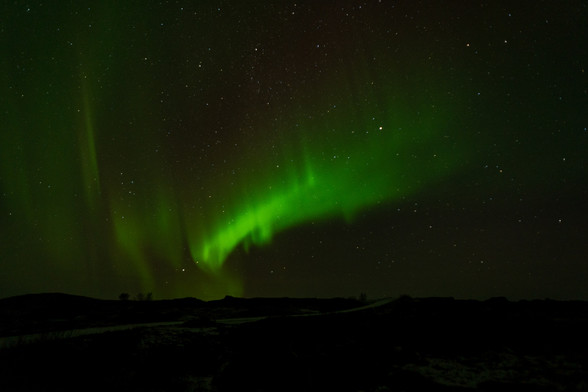Green aurora borealis (northern lights) above a dark landscape