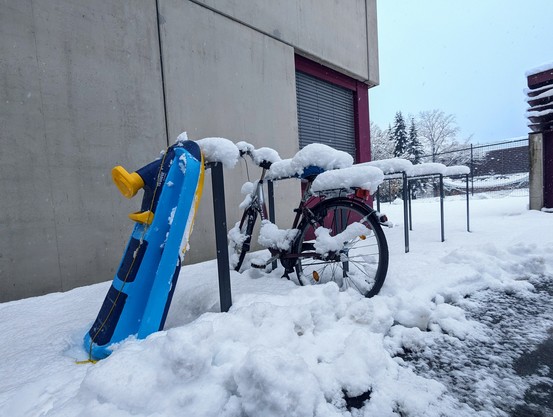 Ein mit dickem Schnee bedecktes Fahrrad an einer unÃ¼berdachten Radabstellanlage - daneben ein Bob, der an einem RadstÃ¤nder lehnt.
