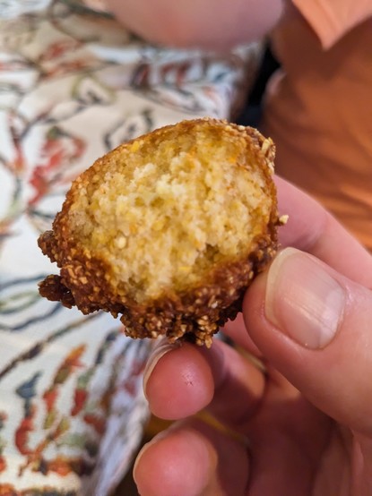 A man's right hand holding a hush puppy with a bite taken out of it