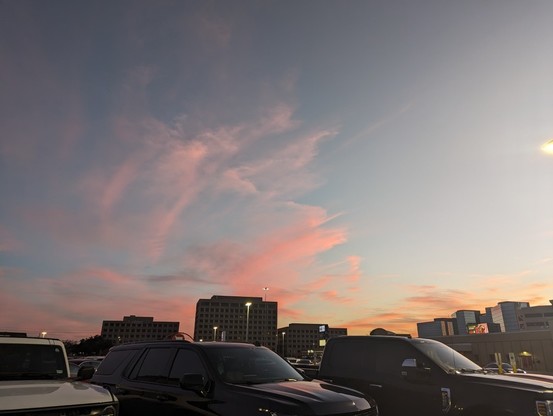 Photo of a sunset over a parking lot. Wispy clouds are painted pink by the sun, which is already out of view.