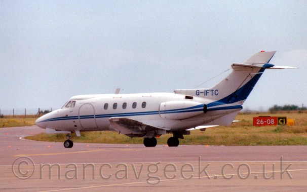 Side view of a white and blue, twin engined bizjet, taxiing from right to left, under a dreary grey sky.
