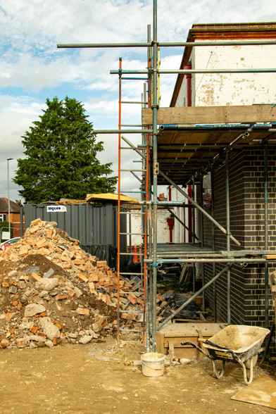 Image of an exterior buildingsite, showing a pile of old bricks on the left and a white building on the right around which scaffolding is erected.
