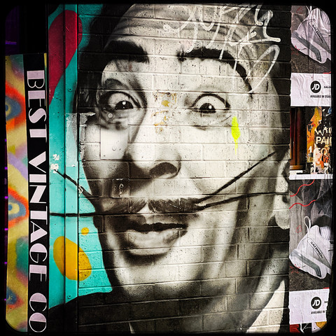 A colour Hipstamatic photo of a piece of street art showing a caricature of Salvador DalÃ­, with a long, thin, forked, waxed moustache