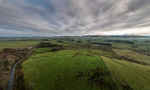 Panoramic wide angle shot over fields and with distant mountains. Cloud covered sky above
