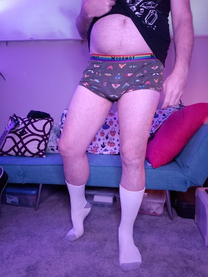 Looking up from the floor at a male figure in his underwear with large feet showing off his tall white socks.