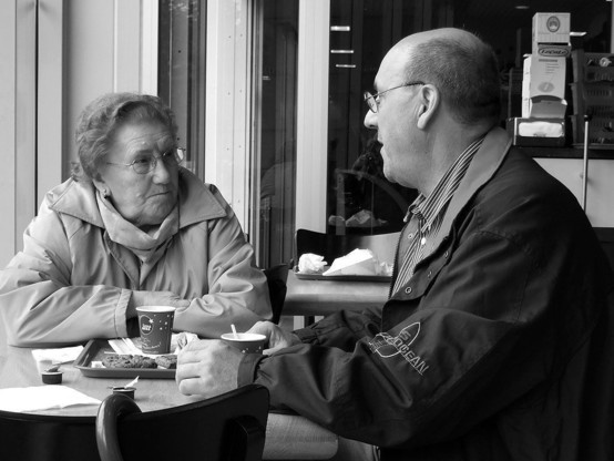 Shared pain is lessened: a black and white photograph of two people in conversation sitting and looking at each other over a cafe table.
