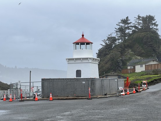 This photograph shows the Trinidad Memorial Lighthouse atop a new permanent foundation. The site is just a short walk from the ocean and the town of Trinidad. In this view, the lighthouse perches on a raised concrete and soil foundation, surrounded temporarily by a chain-link fence while the remaining work is being carried out.