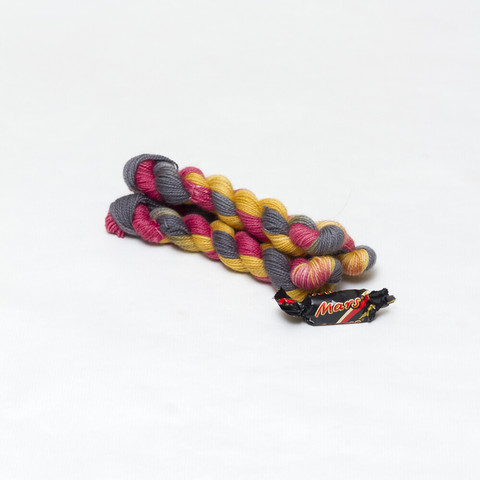 Picture shows three mini skeins of yarn positioned diagonally in a pyramid. The yarn is shades of black, red and gold. To the front of the yarn is a mini Mars foil wrapped sweet.