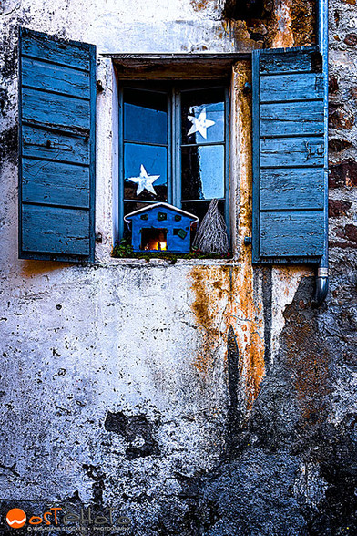 Festively decorated window with blue wooden shutters in Friuli's Poffabro