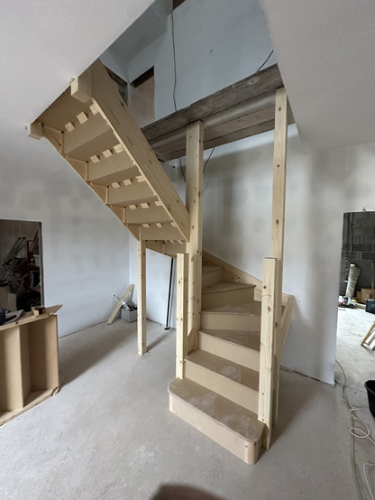 A wooden staircase in a room under construction, featuring bare walls and an unfinished floor.