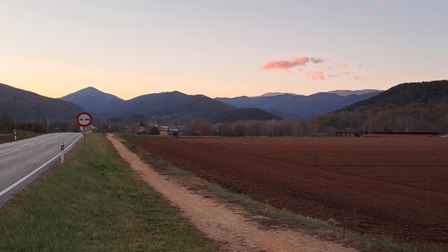 Blick auf Bergketten der Pyrenäen im Licht des Sonnenuntergangs, entlang einer Straße und eines Feldwegs.