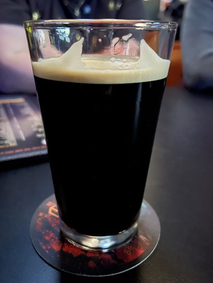 A pint glass of dark beer with a creamy tan head