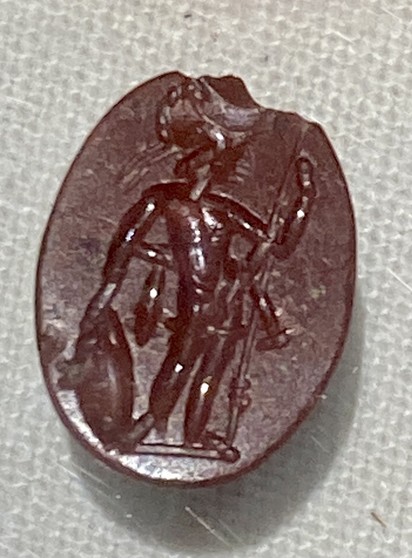 Photo of a red jasper intaglio depicting the Roman war god Mars holding his spear and shield. He is in the nude but wears his helmet.