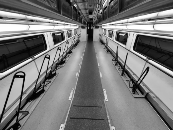 Black and white photograph of the interior of a regional train car where bike storage is available main level for the entirety of the car and no passenger seating. In the distance is the end of the car and the door to the next car.