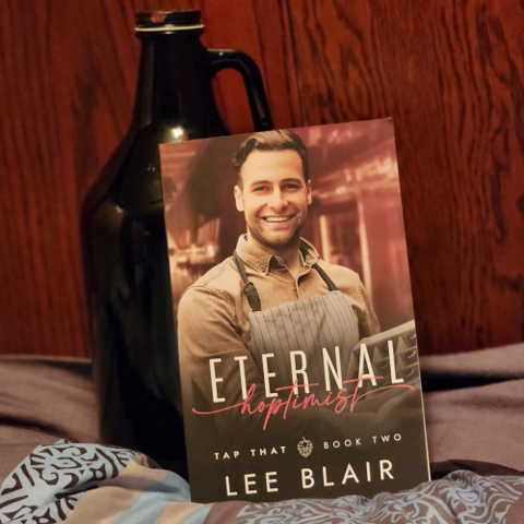 Eternal Hoptimist by Lee Blair, cover a smiling 30-something brunette white man in a long sleeve brown shirt with striped apron holding a case of beer.