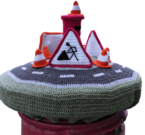A knitted crochet post box topper of some roadwork cones and signs