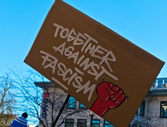 A cardboard sign that reads "Together against facism". A red fist is painted underneath.