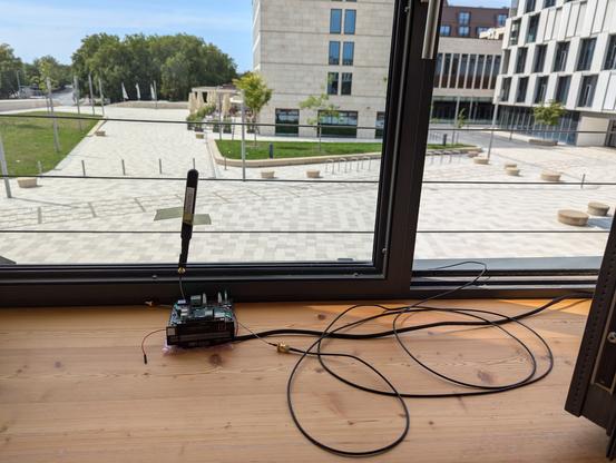 Electronics with some antenna. Installed right at a window. In the background: Some public space, sunny weather.