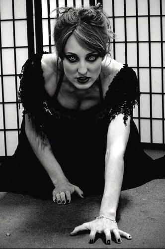 Marina in long black dress, crawling on floor with creepy special FX contact lenses.
Black and white photo. Screen divider panel behind her.
