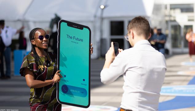 Woman holding a sign that looks like a mobile phone with an incoming call from the future.