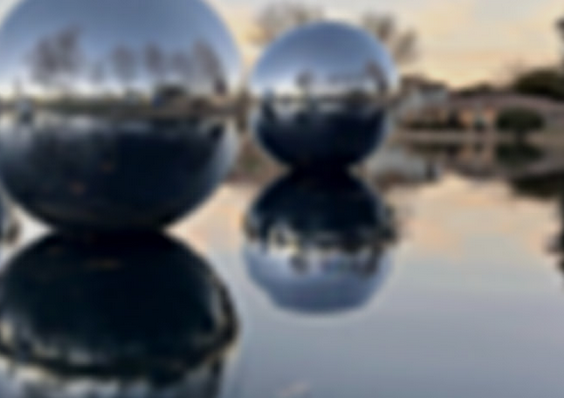 Photo of a lake with silver spheres floating on its surface. The spheres are so shiny that they perfectly reflect the lake and surrounding shore in a very striking psychedelic way.