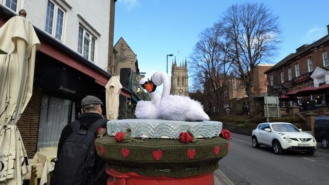Picture of a post box topper of two white swans with intertwined necks. St George's Church is in the background under a clear blue sky.