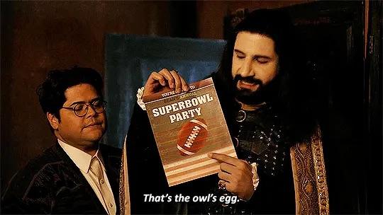 Nandor and Guillermo from “What we do in the shadows”. 

Nandor holds up a A4 sized invitation to a “Super Bowl party” and points to the football pictured on it: “That’s the owl’s egg.”