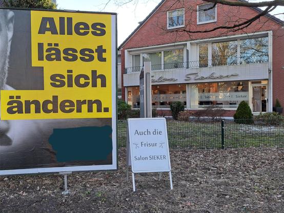 Großes Wahlplakat "Alles lässt sich ändern", ergänzt durch einen Aufsteller "auch die Frisur - Salon Sieker", direkt vor dem Salon Sieker. Die Partei ist unwichtig, daher übermalt.