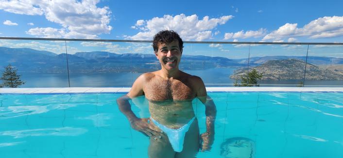 Selfie taken inside an infinity pool overlooking a lake, mountains and cloud filled skies.
