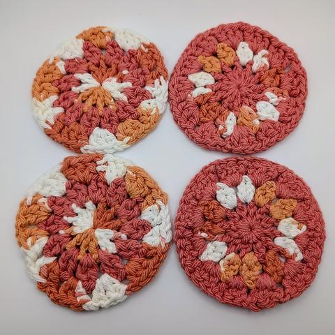 A set of 4 crocheted coasters in salmon and a multicolor yarn that is shades of orange and white.