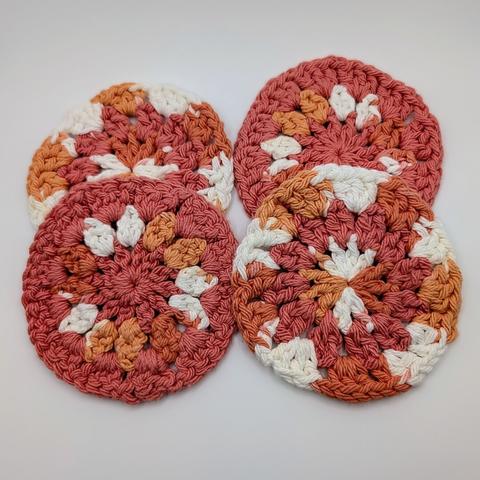 A set of 4 crocheted coasters in salmon and a multicolor yarn that is shades of orange and white.