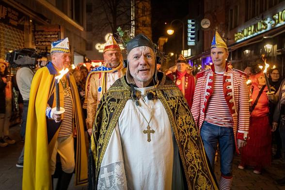 Nachtaufnahme einer Gruppe von Männern in Karnevalskostümen. angeführt von einem älteren Herrn in Priestergewand