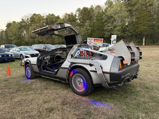 A DeLorean modified to look like the time machine from Back to the Future with glowing lights, gull-wing doors open, and a flux capacitor.