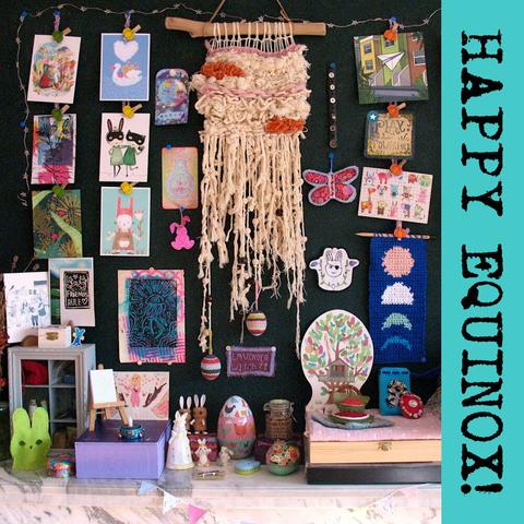 Altar set-up on mantlepiece with lots of small bunny statues, wooden boxs, a treehouse calendar, and decorated egg. On the wall is a woven wall hanging surrounded by postcards, mainly featuring bunnies, and a self-made fabric butterfly and a blue crochet wall hanging with the phases of the moon.