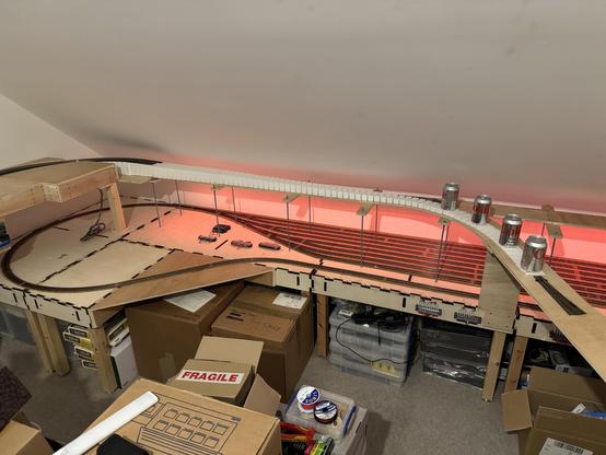 A wide shot of the railway layout under construction. Across the back is the newly installed foam inclined, held in place elite it dries with cans of Diet Coke