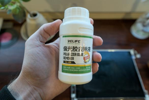 Photo of a white bottle called "Polarizer Glue Remover"  with the number 8222 alongside it, held in my hand, and with the PowerBook's display seen laying in the blurry background.