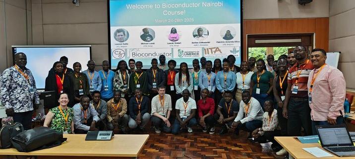 Bioconductor Nairobi course group photo on ILRI campus in workshop room, under slide saying welcome to Bioconductor Nairobi course showing photos of instructors and organiser and funder logos.
