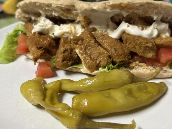 Kebab made with marinated soya chunks, lettuce, tomato and vegan mayo, with pickled jalapeños on a white plate.